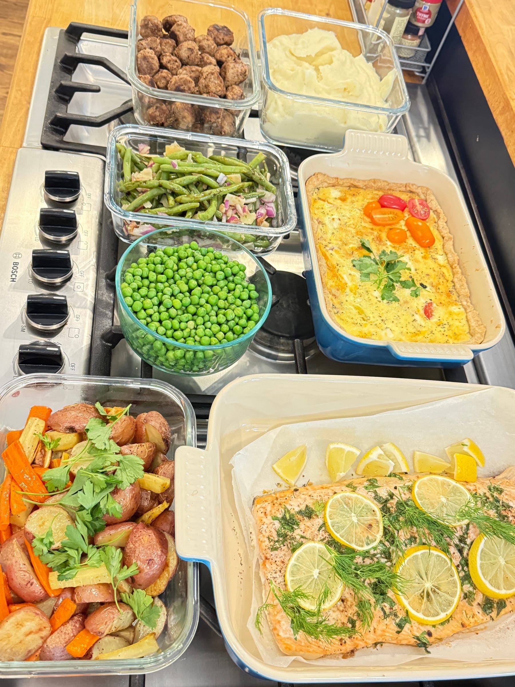 The same week portioned into glass containers — lemon-dill salmon, quiche, Swedish meatballs and vegetable sides