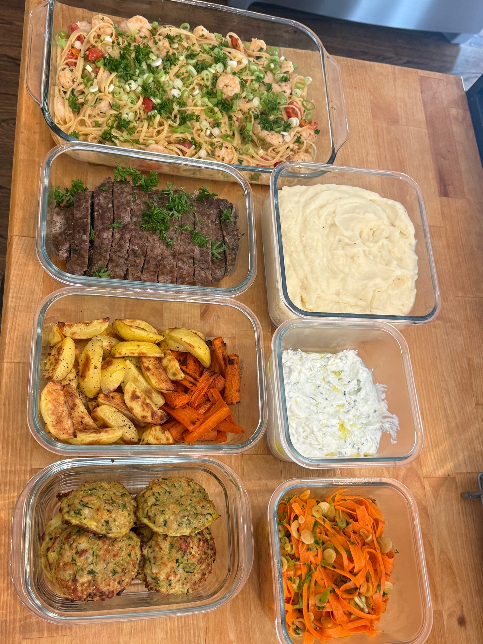 A finished week in glass containers — shrimp scampi, seared steak, roasted potatoes and carrots, coleslaw, herb fritters and carrot salad